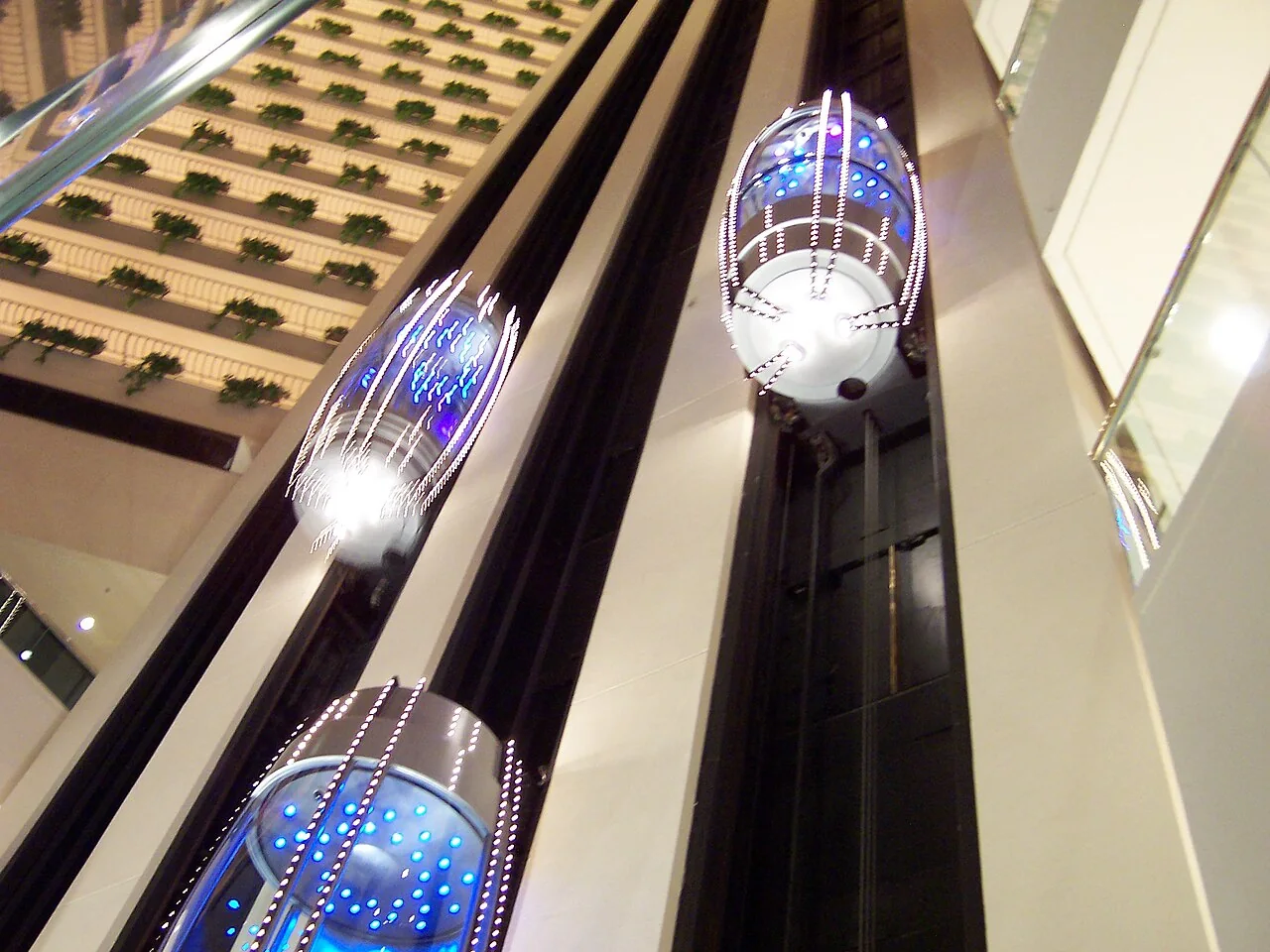 Glass lift cars with blue lights line the tall shafts of a hotel atrium.
