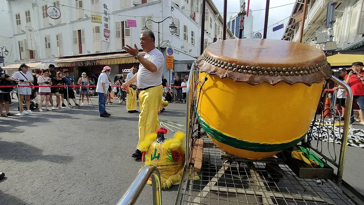 A large yellow lion-dance drum rests on a cart beside a performer.