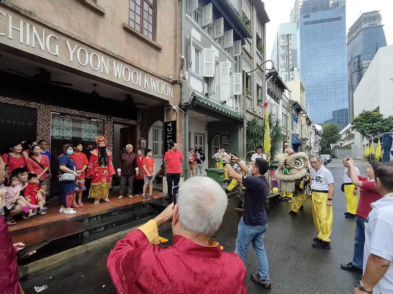 A lion-dance troupe performs on a street as people watch and take photos.