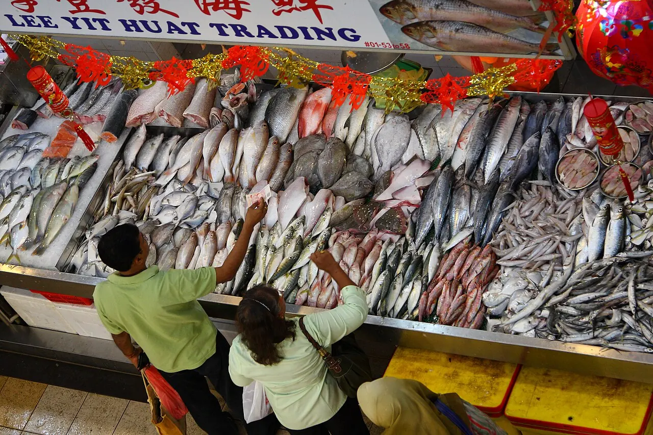 Two people reach toward a display of fish arranged on ice at a market stall.
