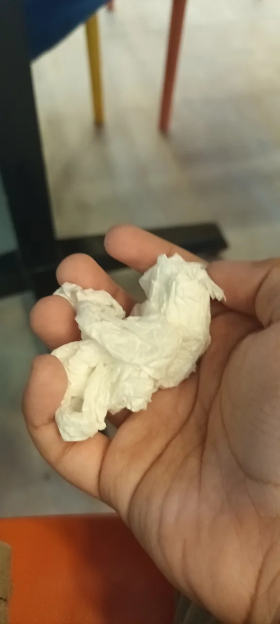 A hand holds a small ball of crumpled white tissue paper.