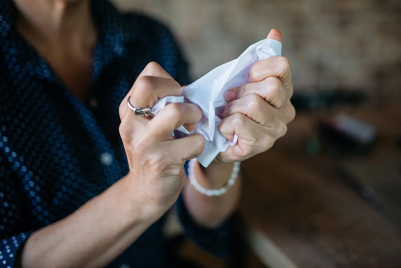 Hands crumple a piece of white paper.