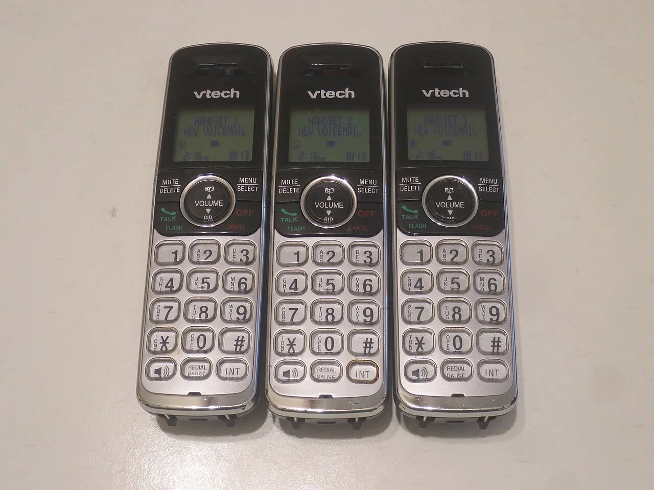 Three black-and-silver cordless phone handsets lie side by side.
