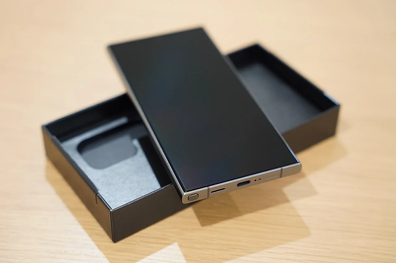 A smartphone with a dark screen rests on its open box.