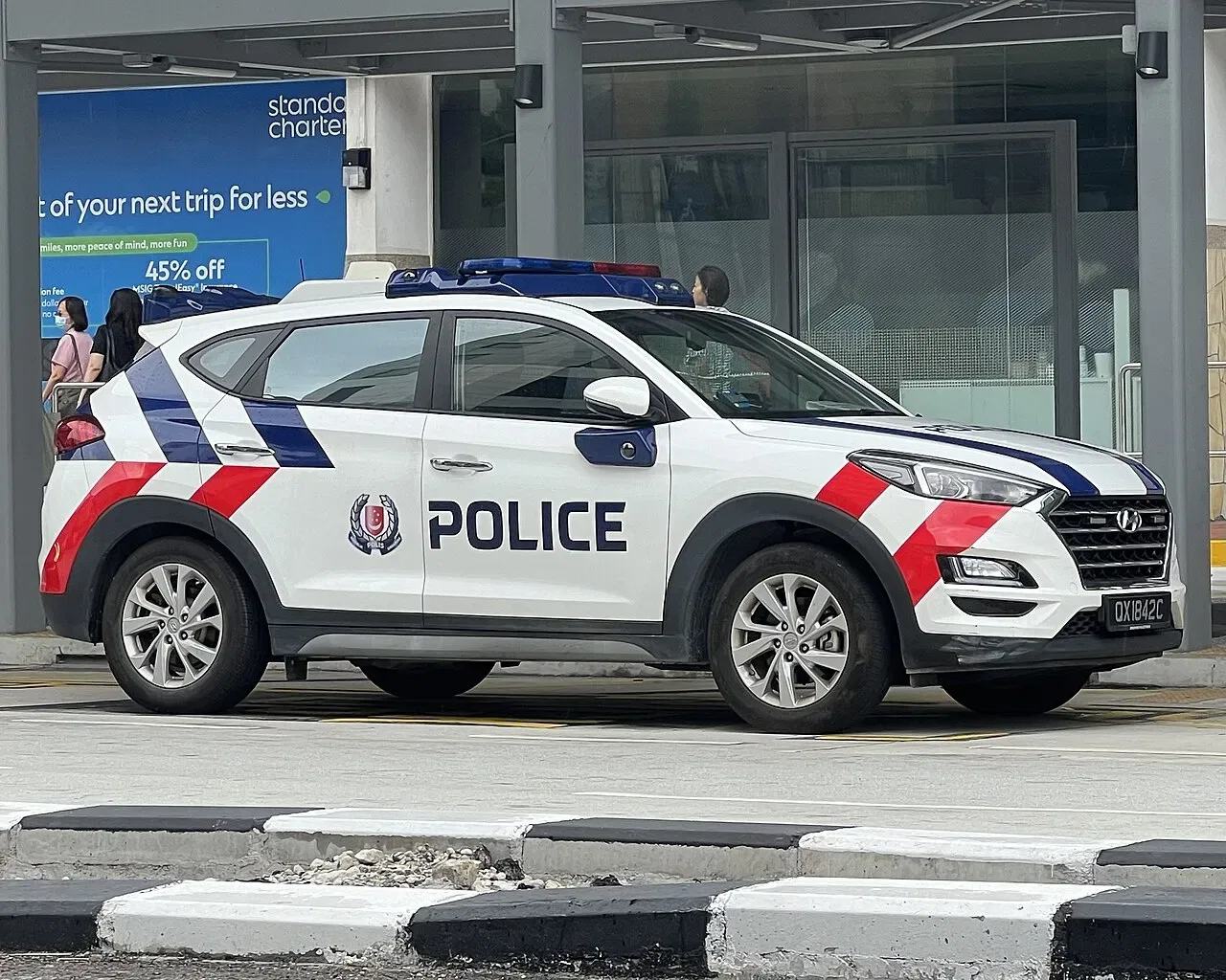 A white police car with red and blue markings and a roof light bar parked on a road.
