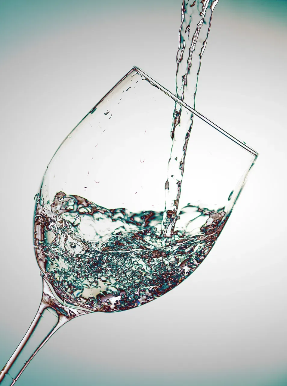A clear stream of water is poured into a tilted wine glass against a plain background.