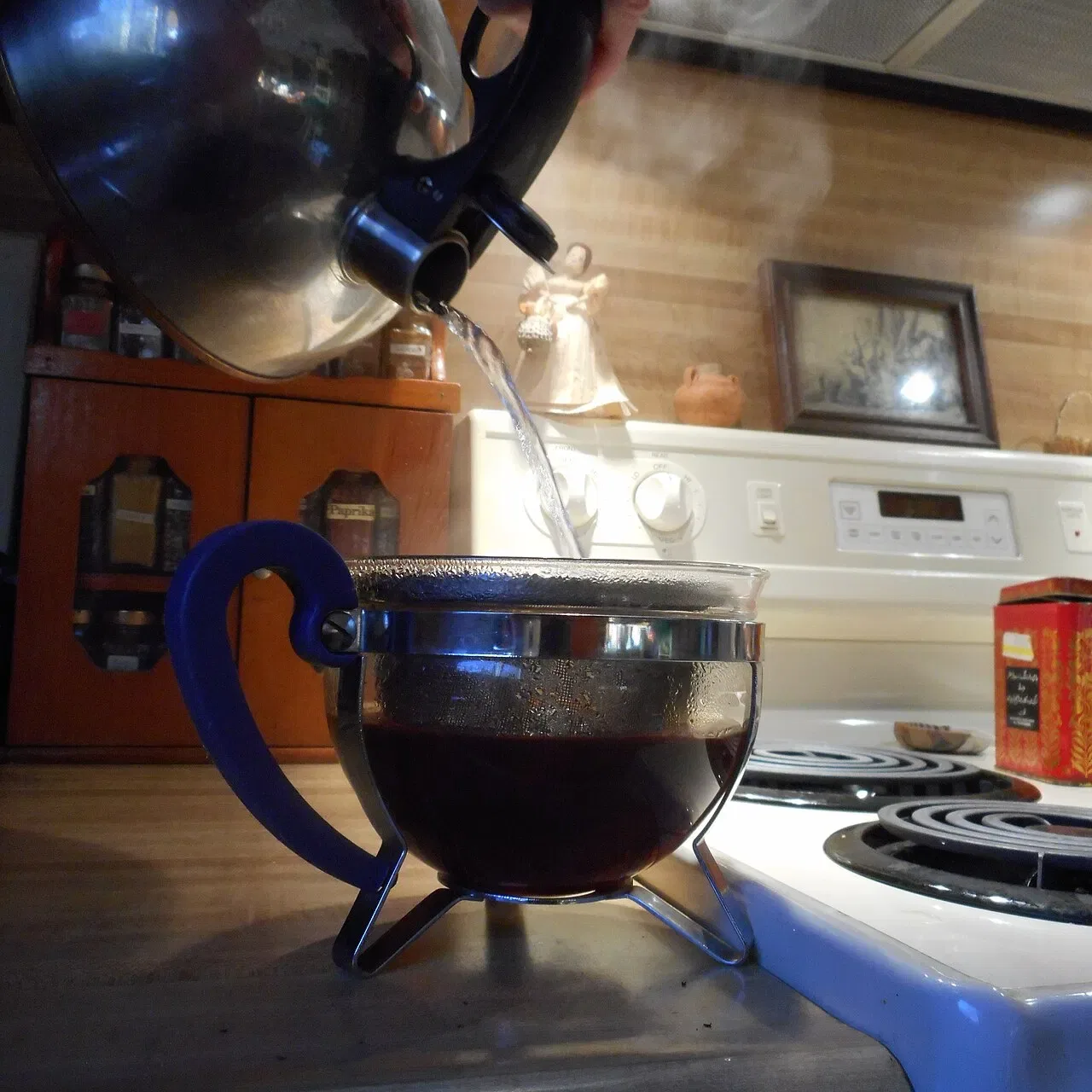 A kettle pours steaming water through a filter into a glass pot.