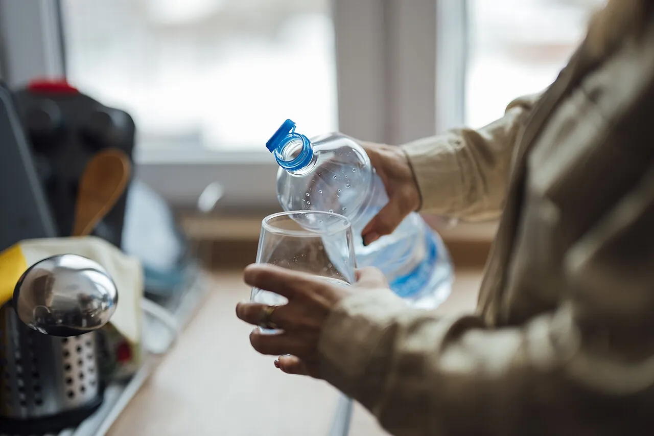A person pours water from a bottle into a glass.