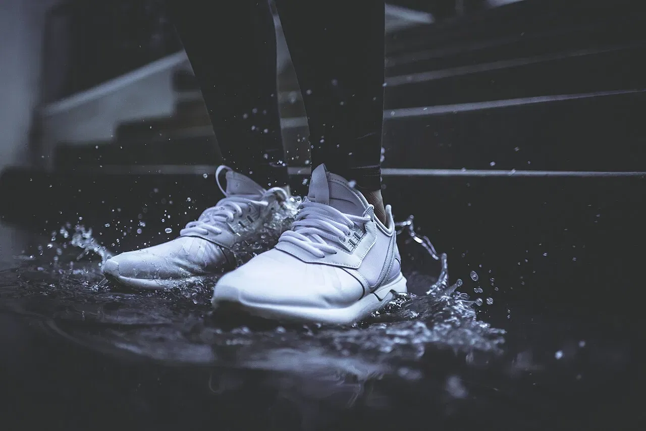White sneakers step into a puddle, splashing water outward.
