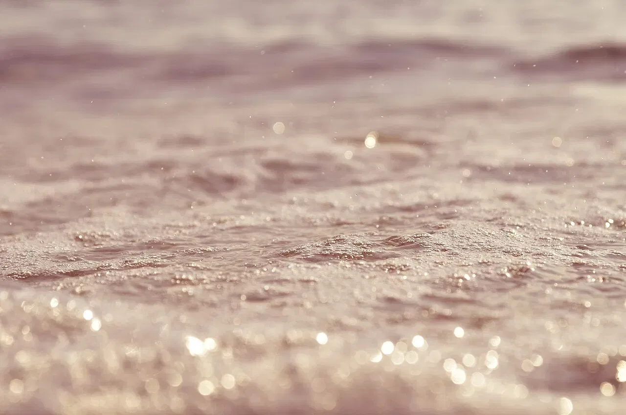 Raindrops fall onto rippling water that sparkles with soft light.