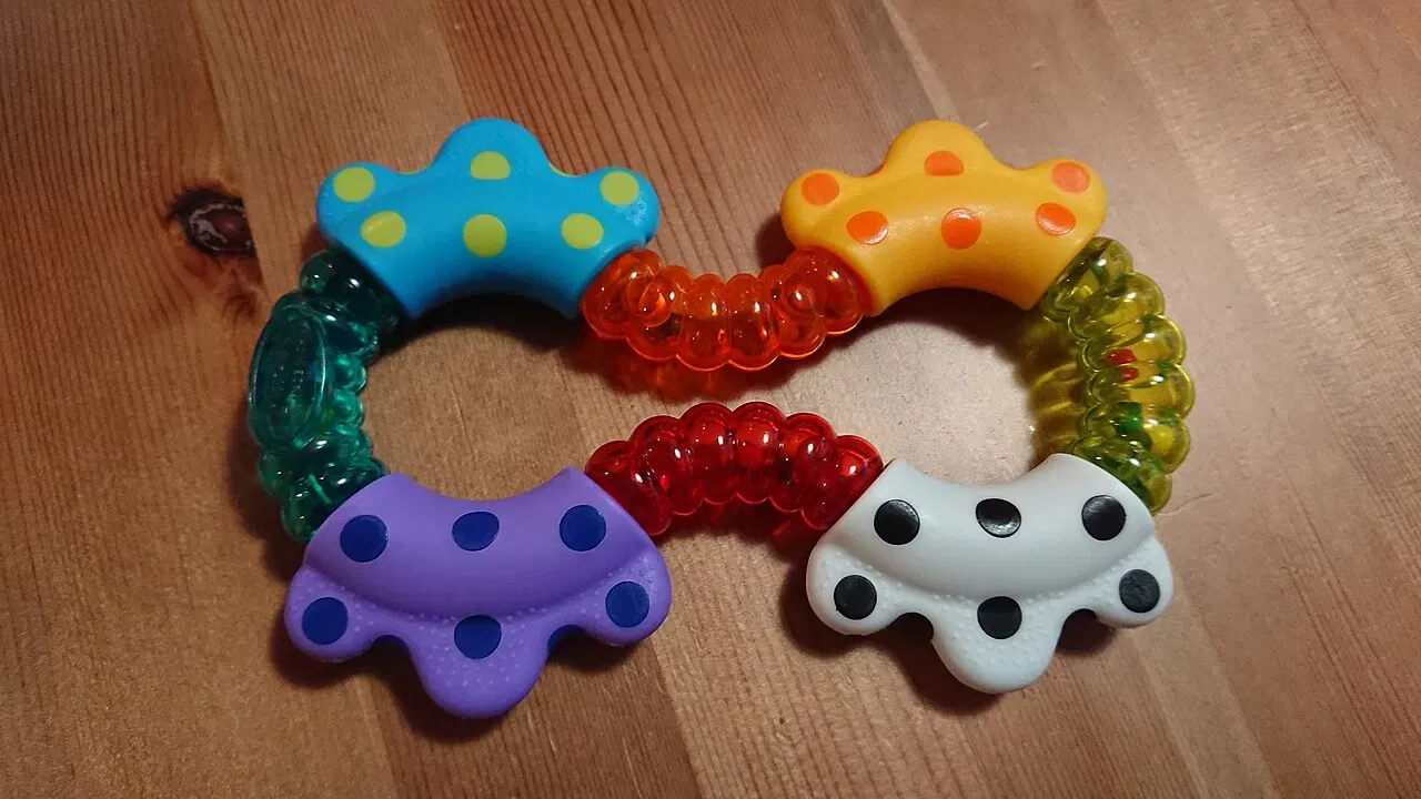 A colourful figure-eight-shaped baby rattle rests on a wooden surface.