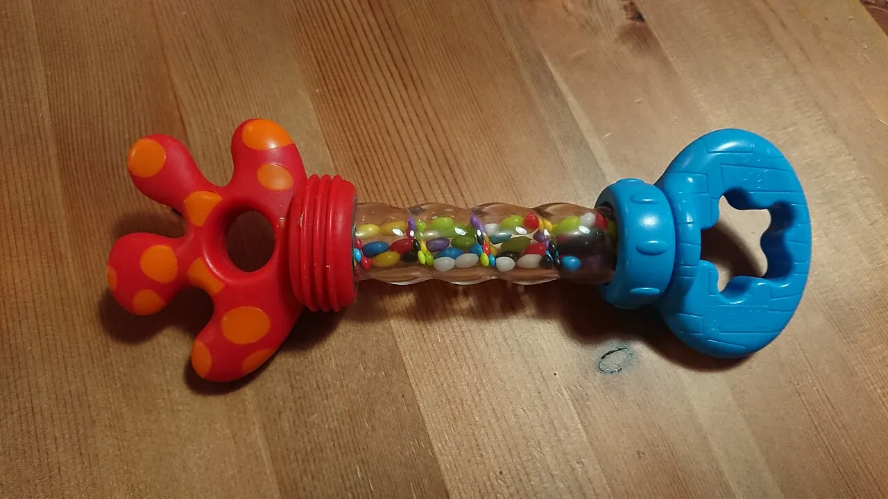 A colourful baby rattle lies on a wooden floor.