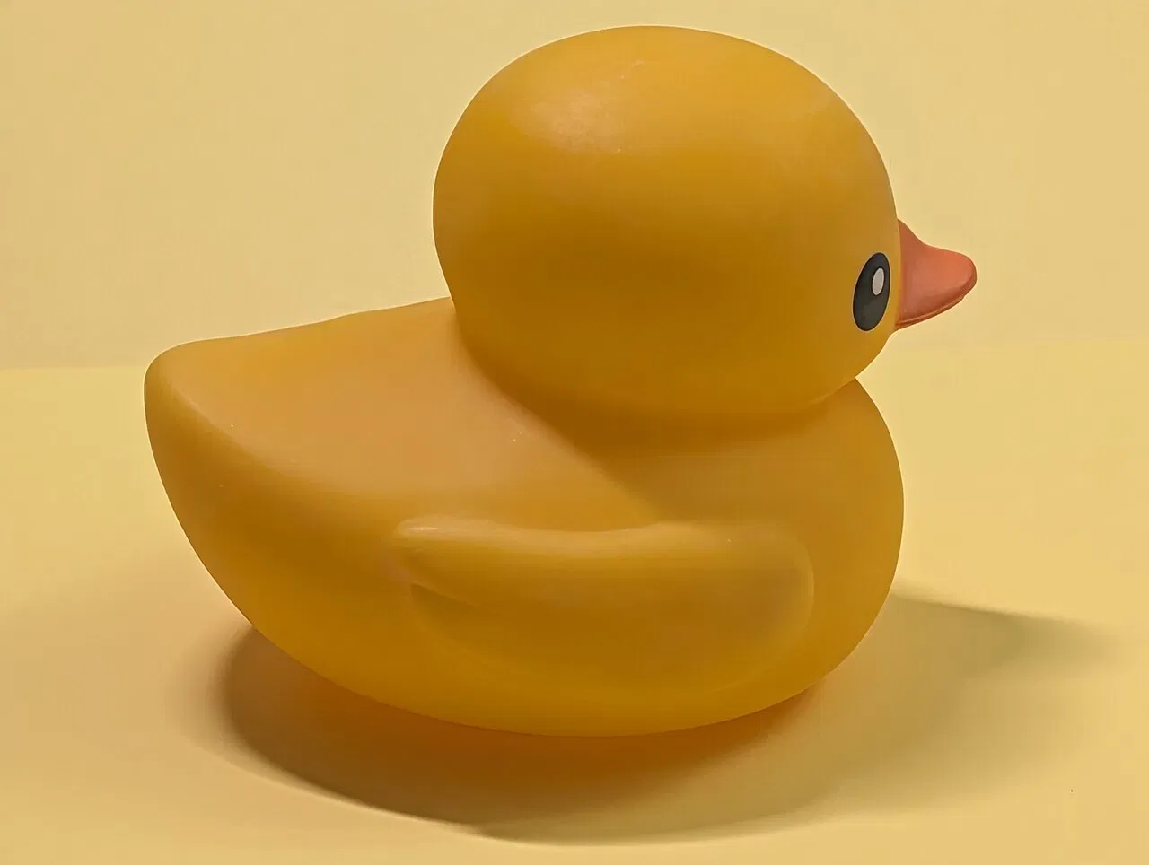 A yellow rubber duck sits against a plain yellow background.