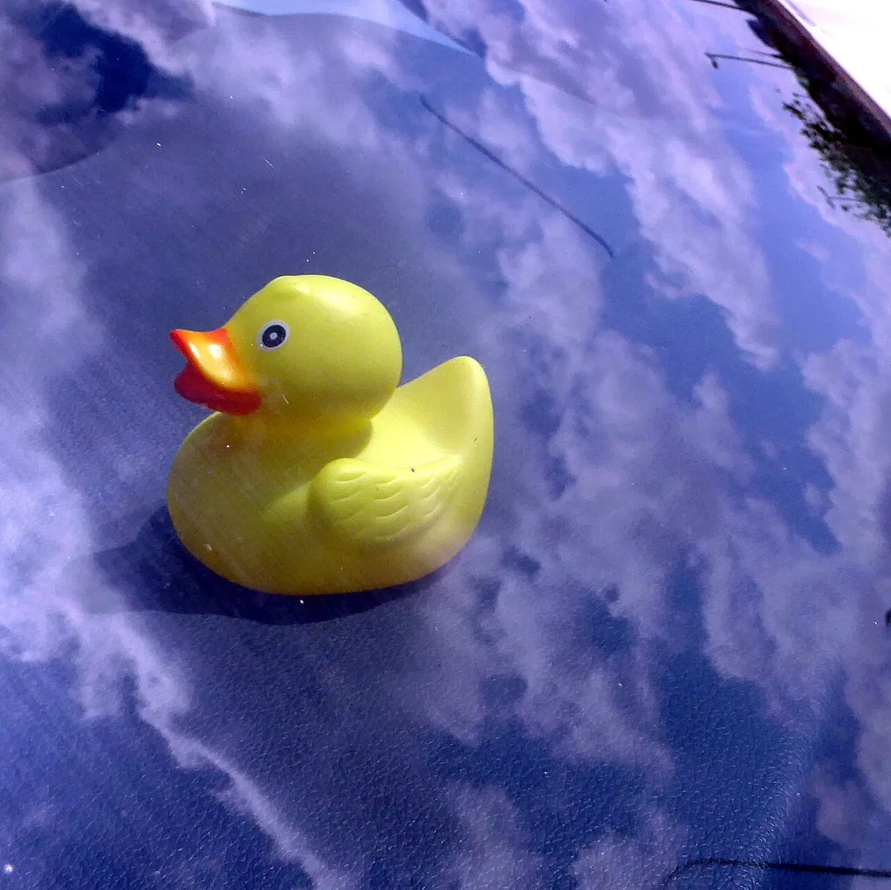A small yellow rubber duck rests against a blue background patterned with clouds.