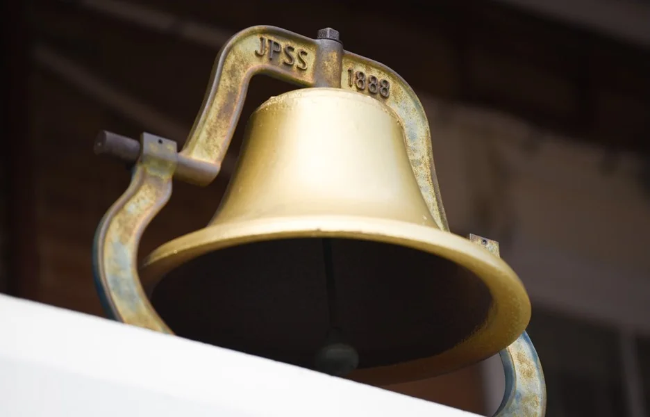 A brass school bell hangs from a curved metal bracket.
