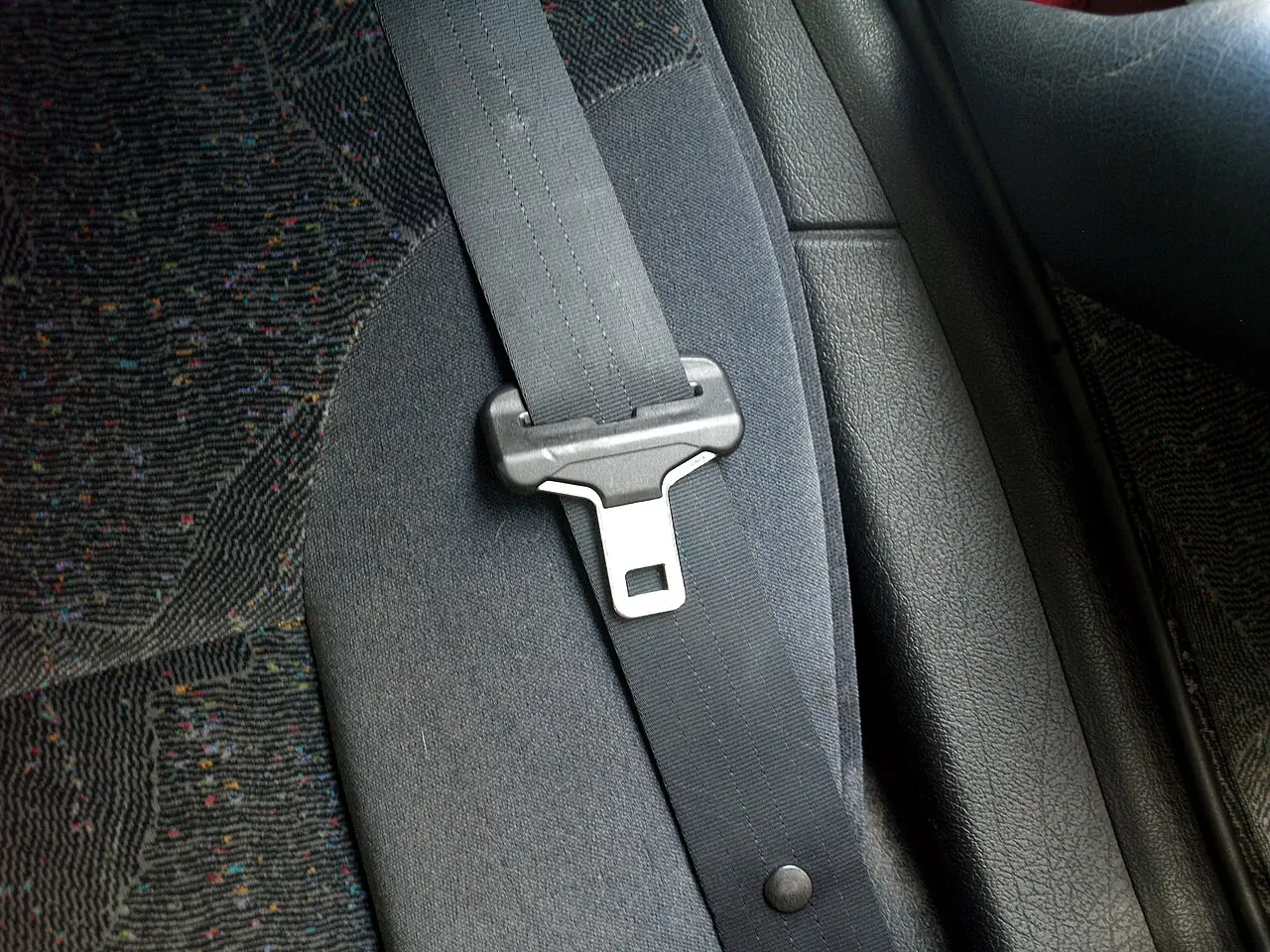 A grey seat belt with a metal buckle lies across a patterned car seat.