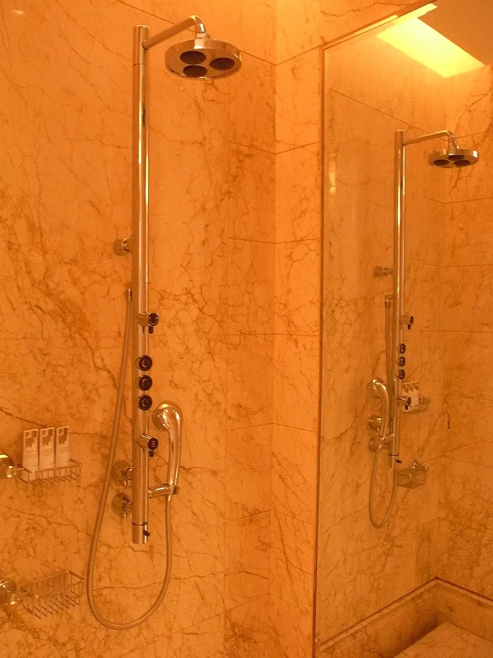 A chrome shower panel with a round showerhead is mounted on a marble wall.
