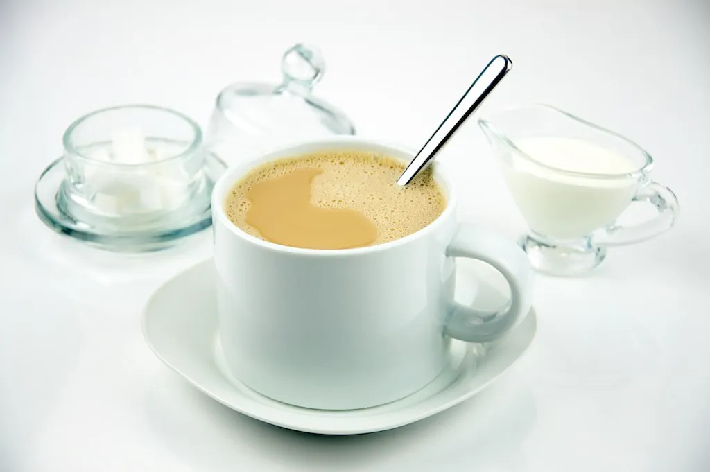 A spoon stands in a cup of light brown drink.