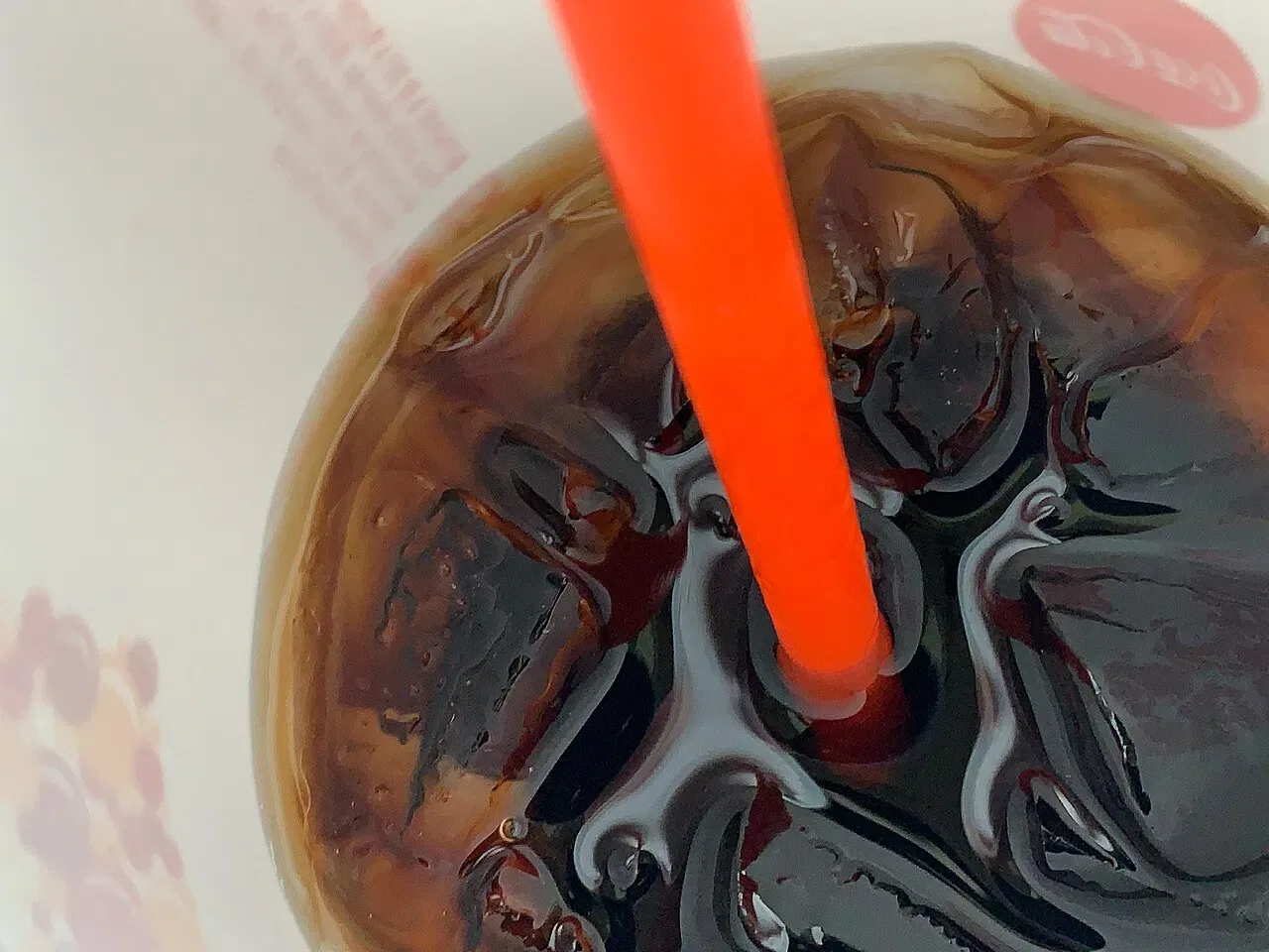 A red straw stands in a dark iced drink in a cup.