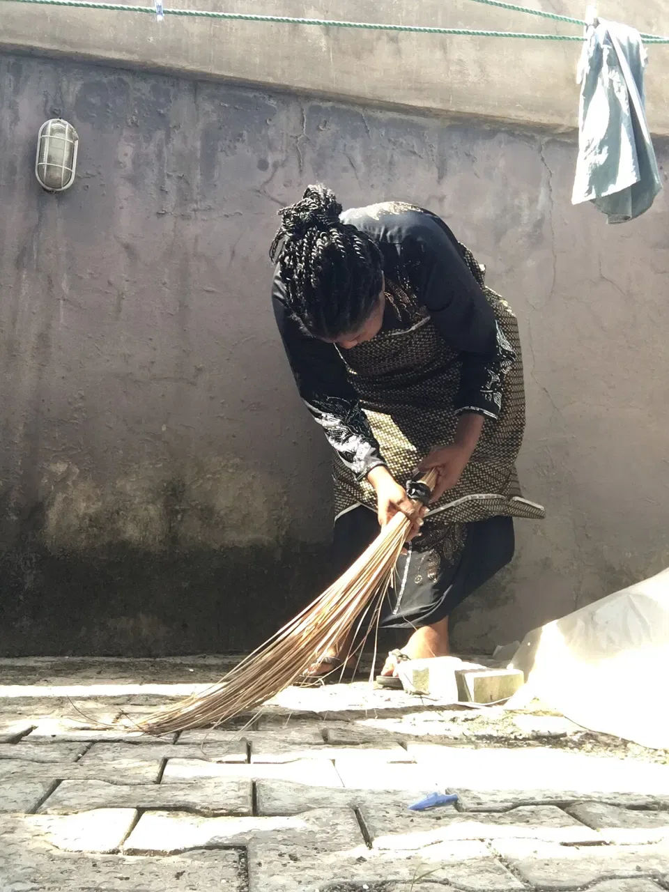 A person bends forward to sweep a paved floor with a bundle broom.