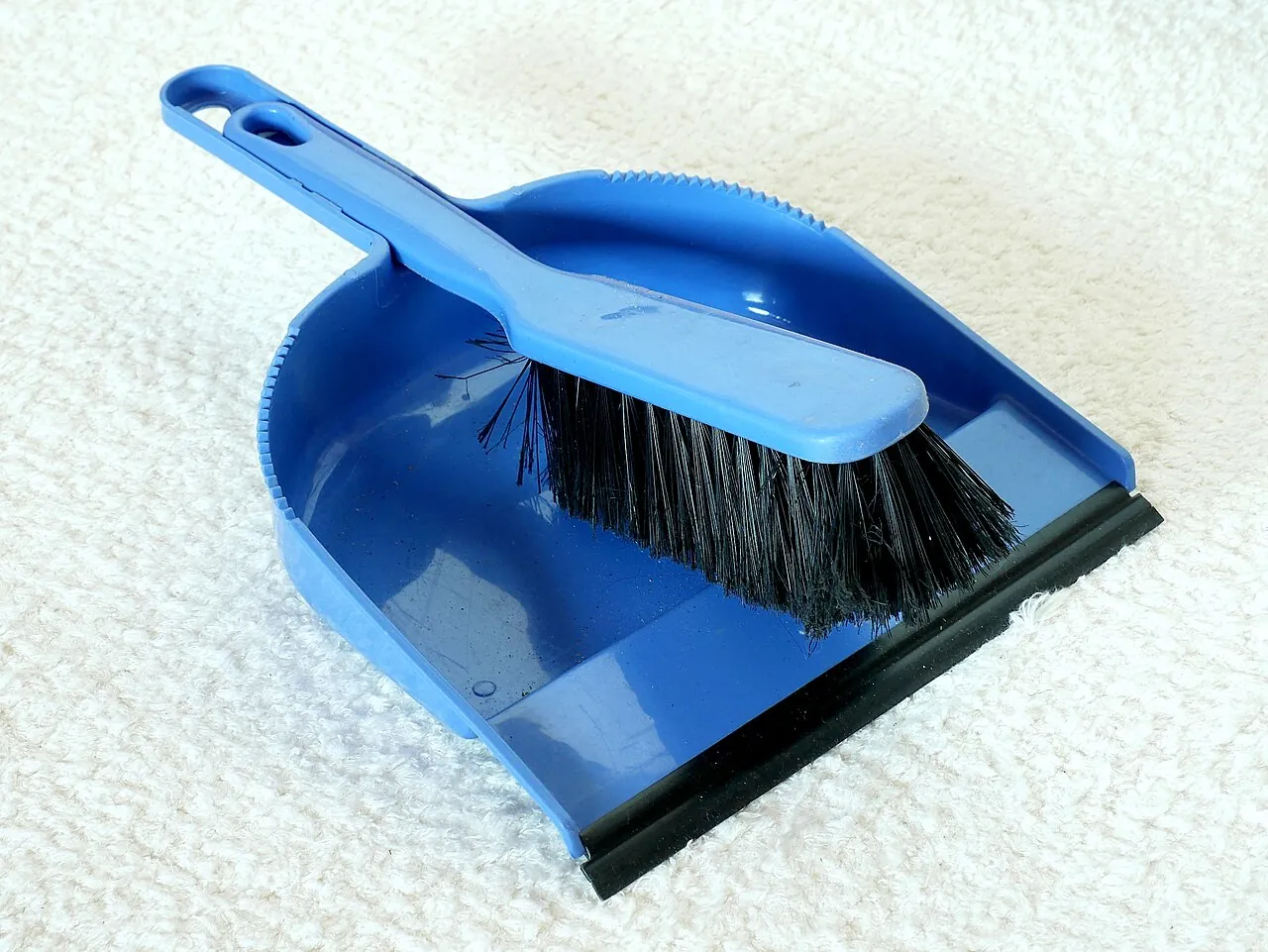 A blue dustpan and brush lie on a pale floor.