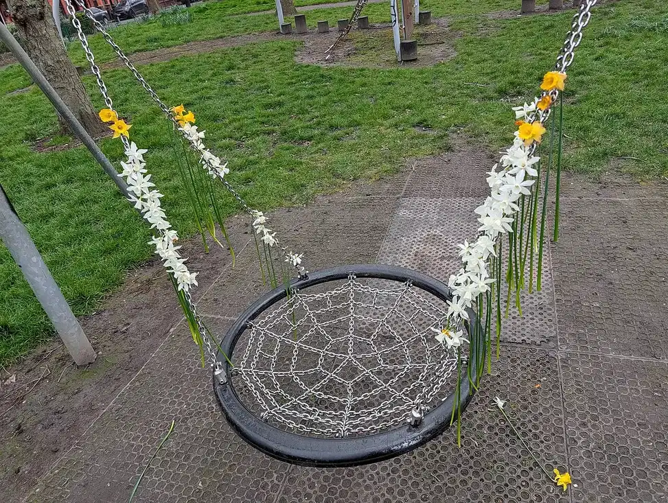 Yellow and white flowers decorate a playground swing with a circular chain-net seat.