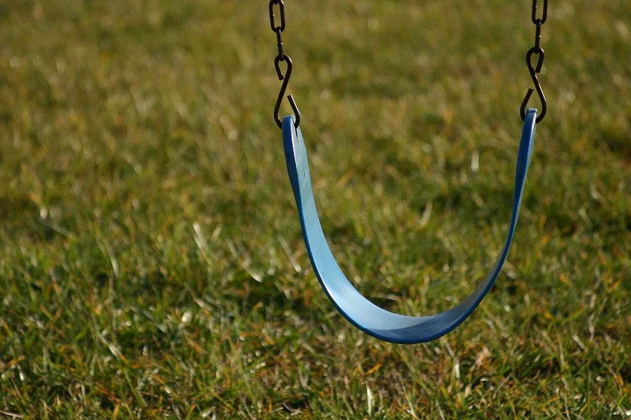 An empty blue swing hangs above grass.