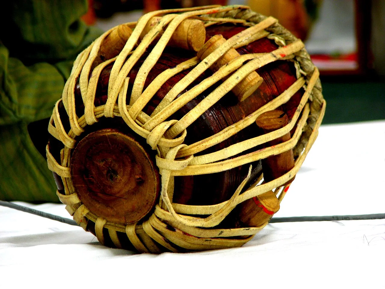 A single tabla drum with a wooden body and leather lacing rests on a white surface.