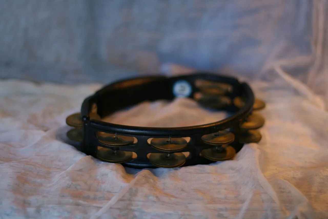 A black tambourine rests on soft fabric.