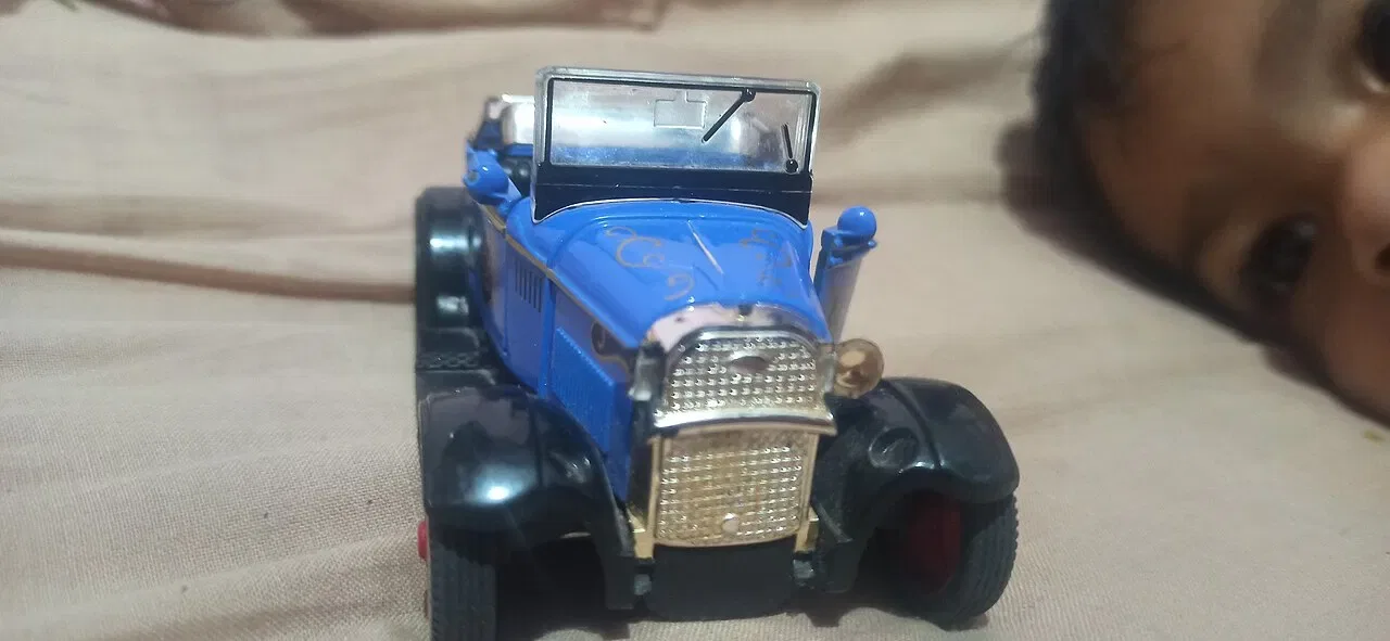 A blue toy car with a chrome grille sits on a beige fabric surface.