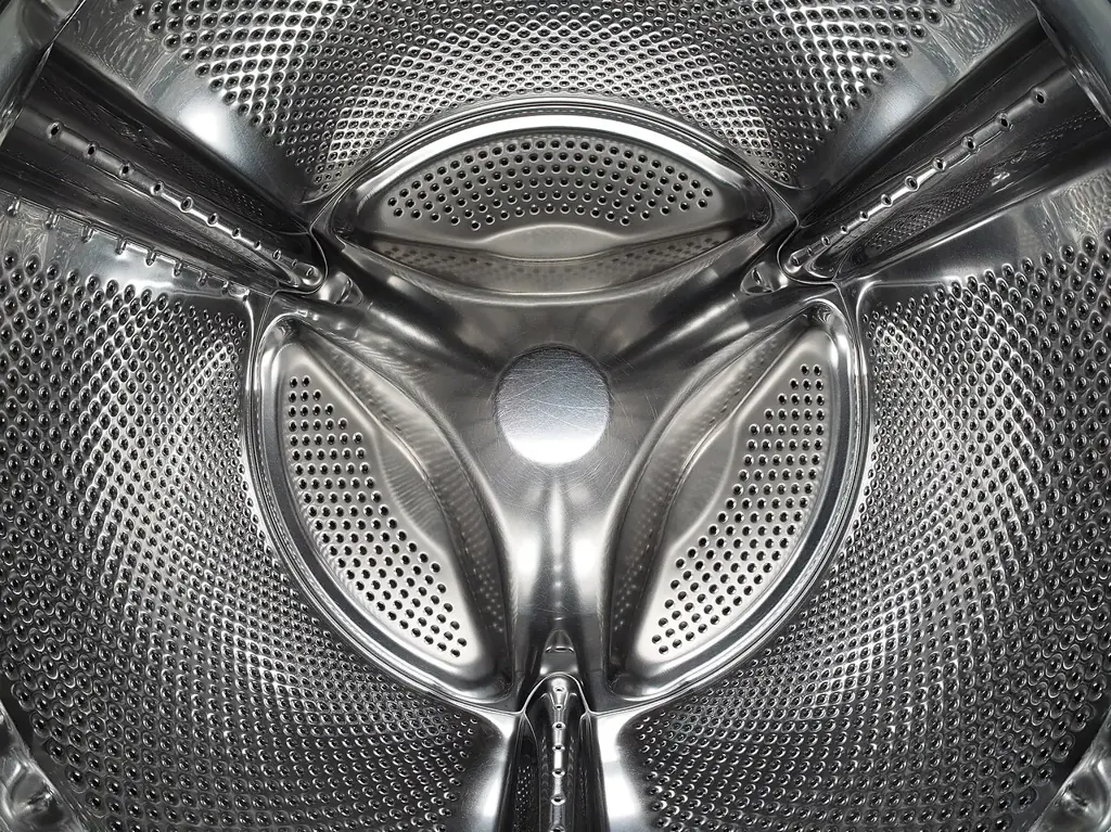 A close view inside a washing-machine drum shows shiny walls dotted with holes.