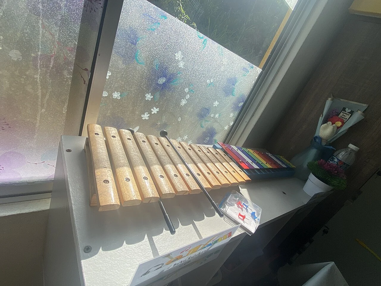 A wooden xylophone and two mallets sit beside a smaller colourful instrument.