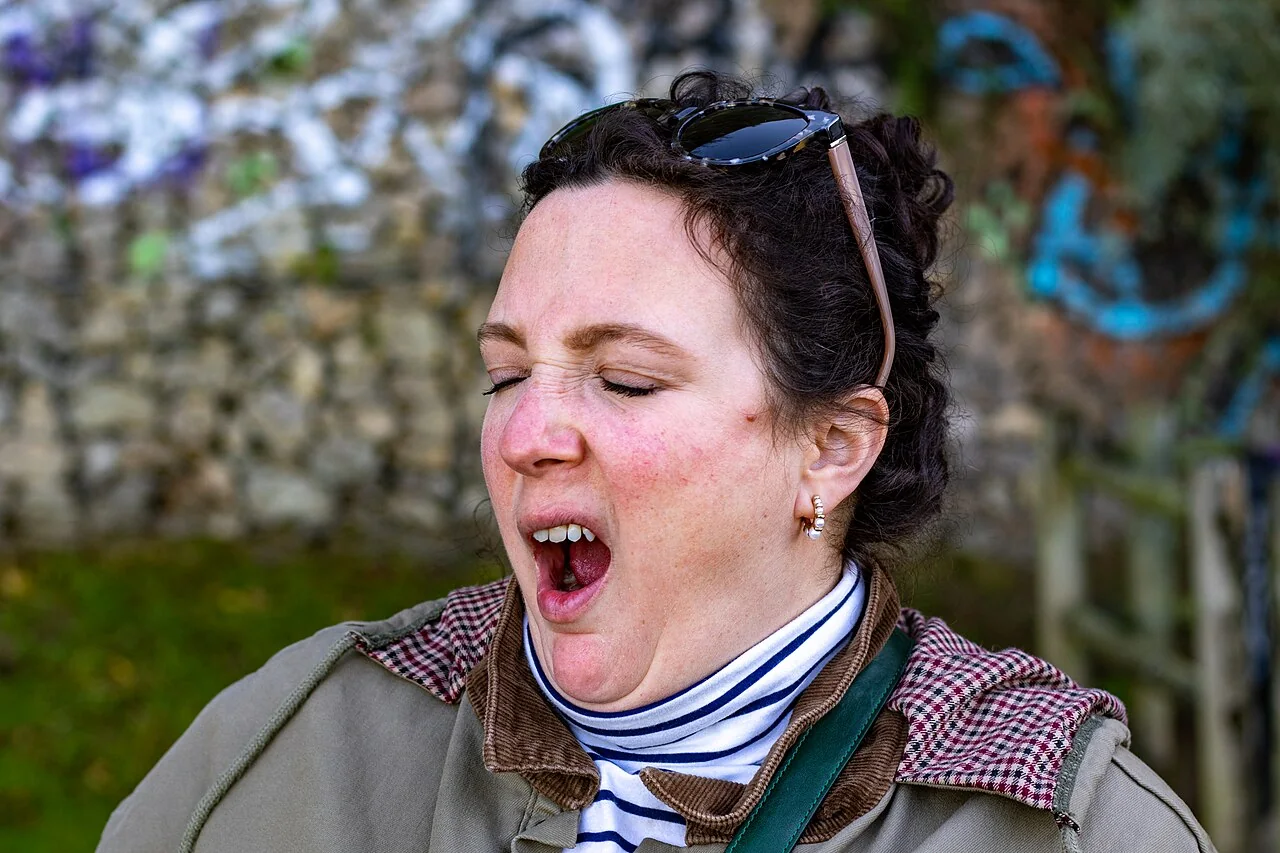 A woman wearing a jacket yawns with her eyes closed.