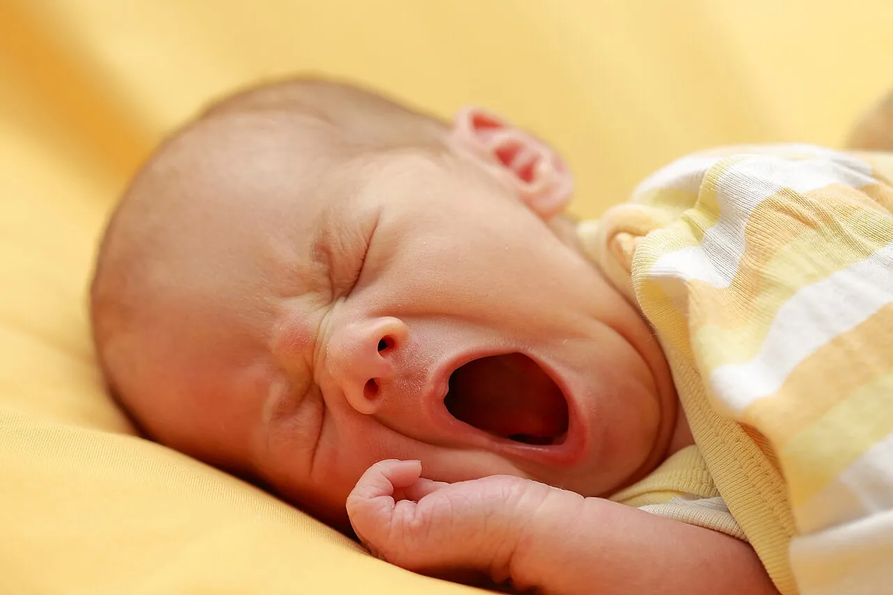 A baby lies down with its mouth open.