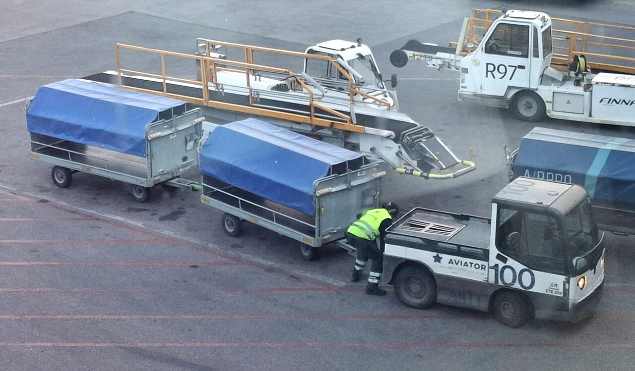 A small white tractor sits beside baggage carts covered with blue sheets.
