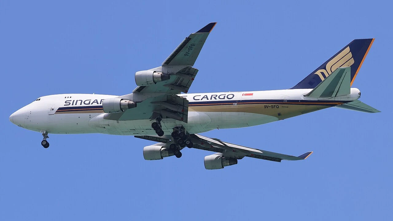 A cargo aircraft is seen from below with its landing wheels lowered.