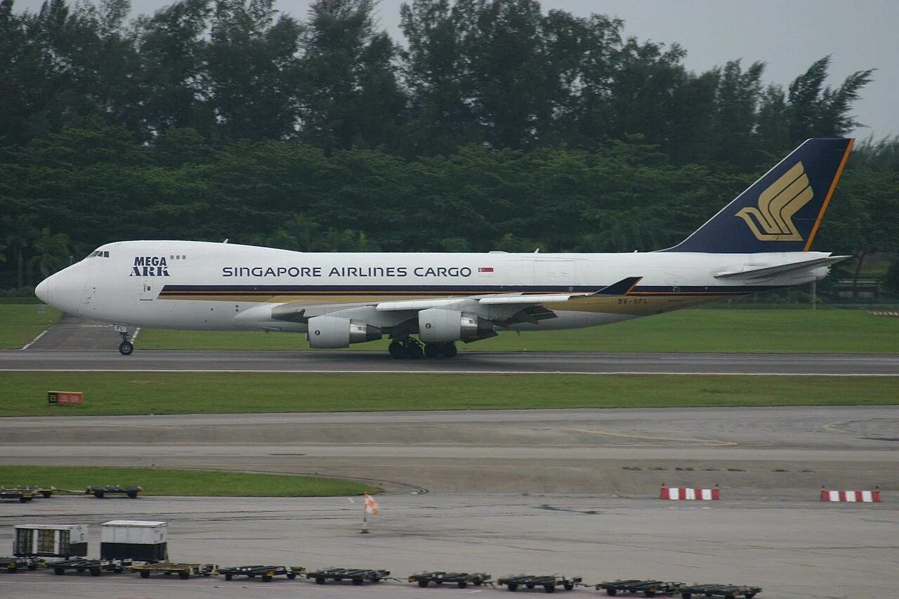 A white cargo aircraft has four engines and a dark blue tail with a gold emblem.