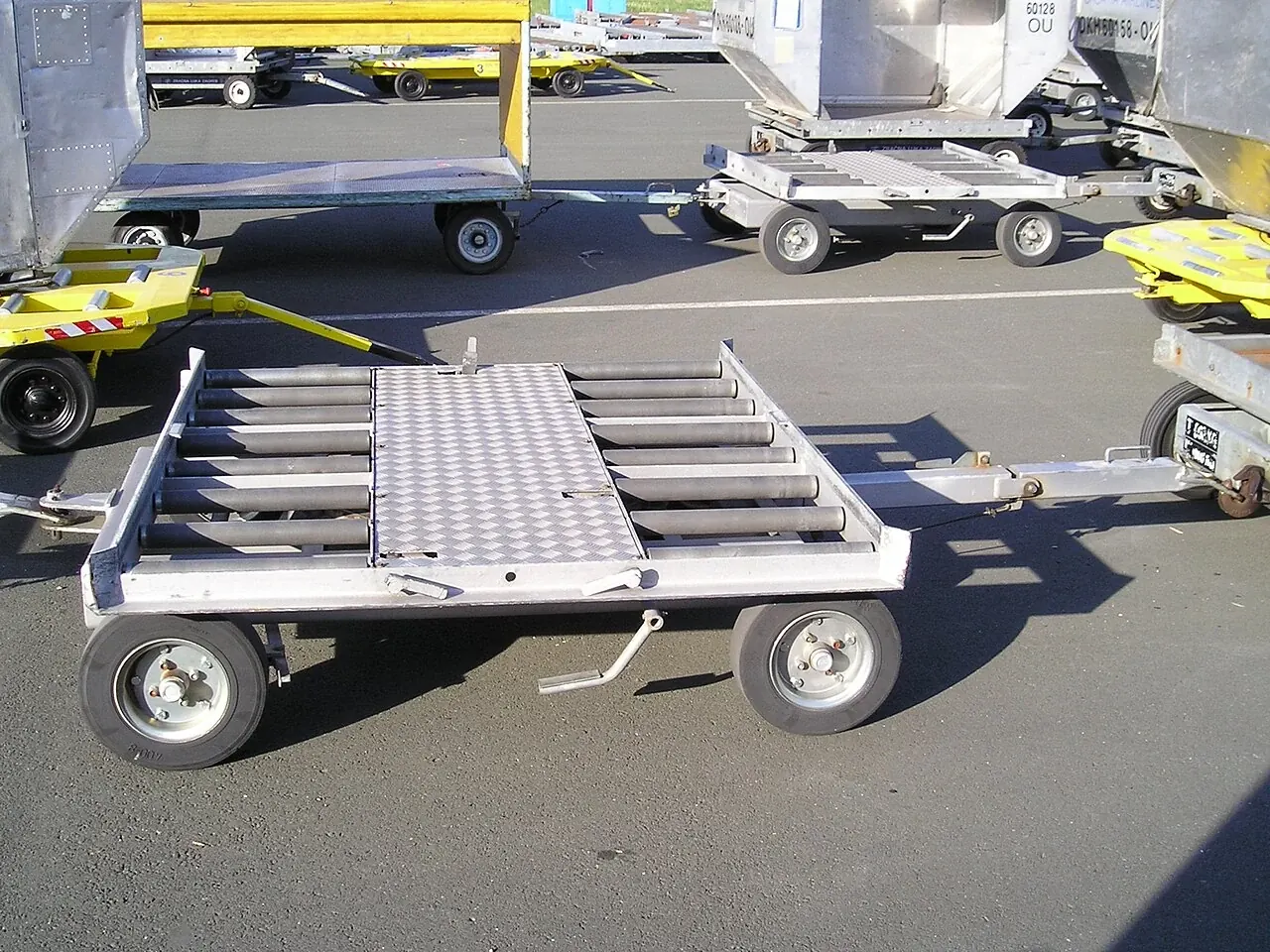 A low silver cargo dolly has four wheels and rows of rollers on its deck.