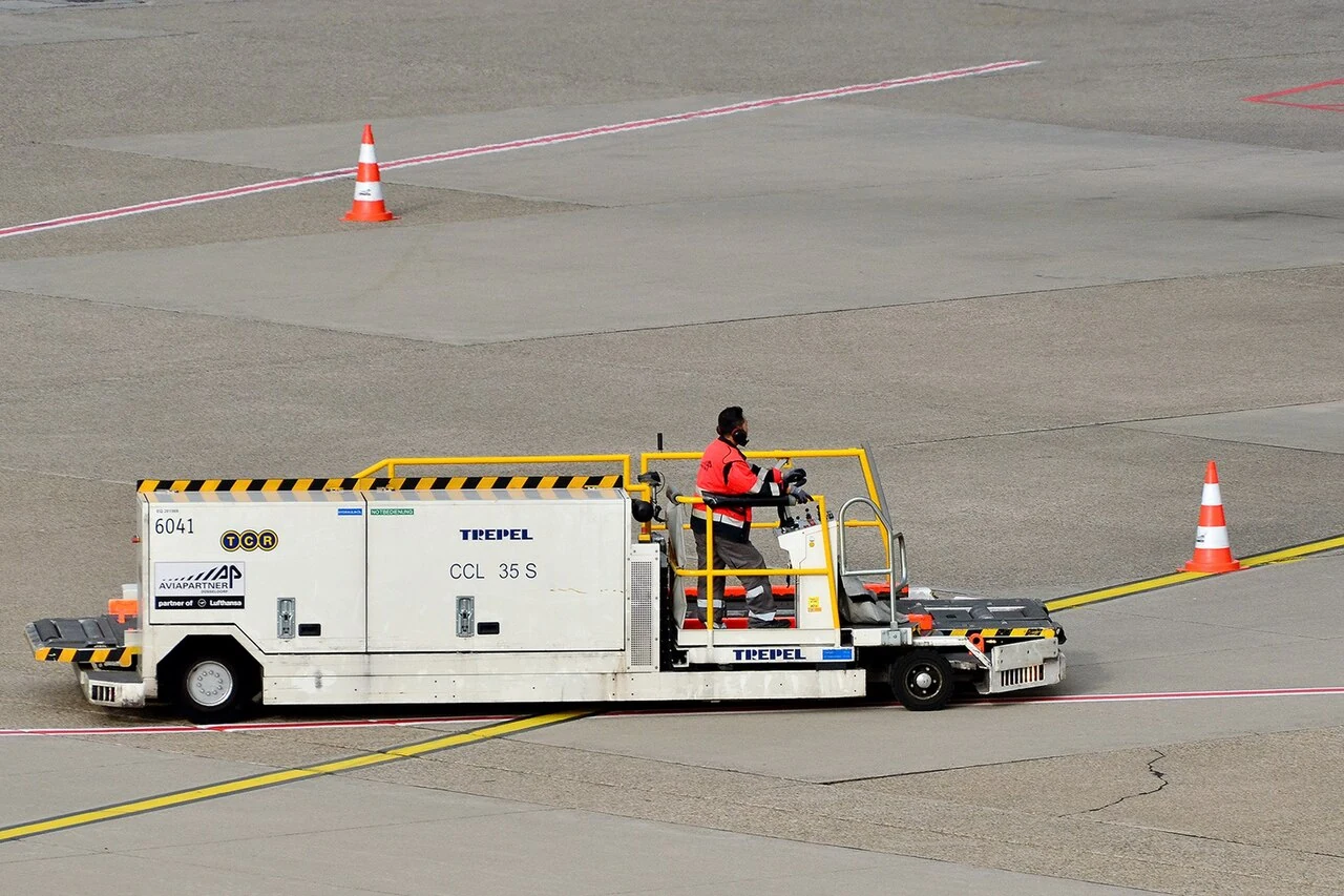 A low white cargo loader has a yellow-railed driving platform at one end.