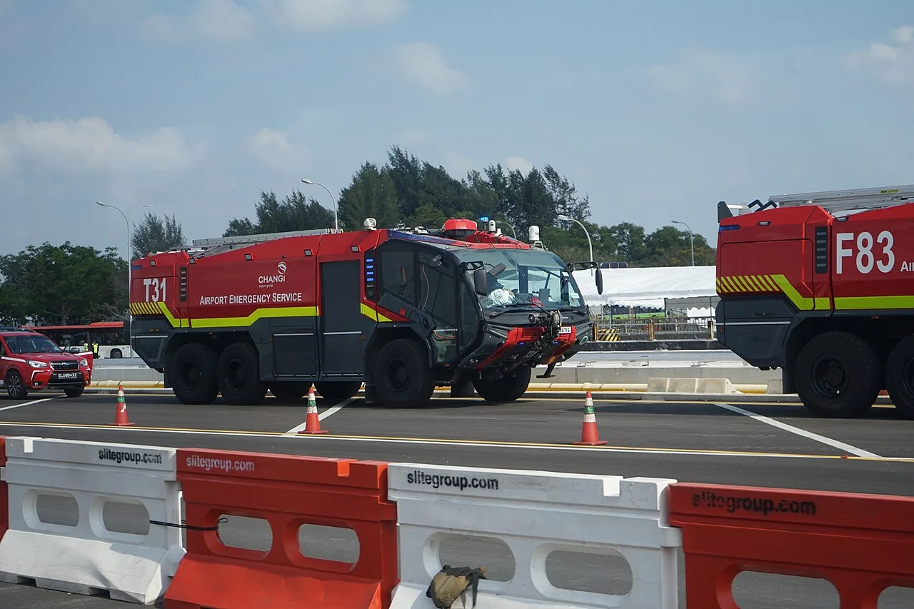 A large red airport fire engine stands beside other emergency vehicles.
