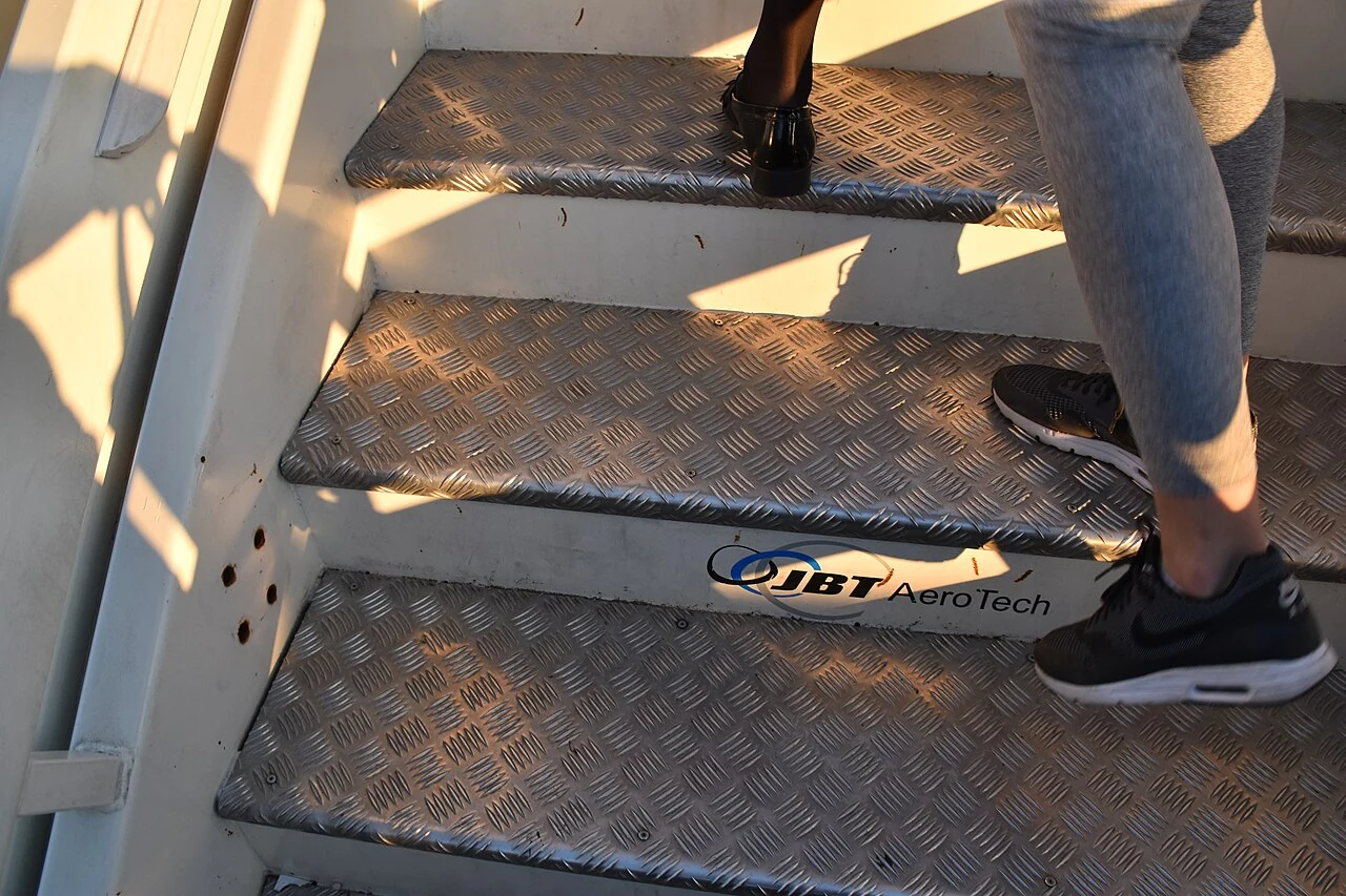 A close-up shows passengers' shoes on textured metal aircraft steps.