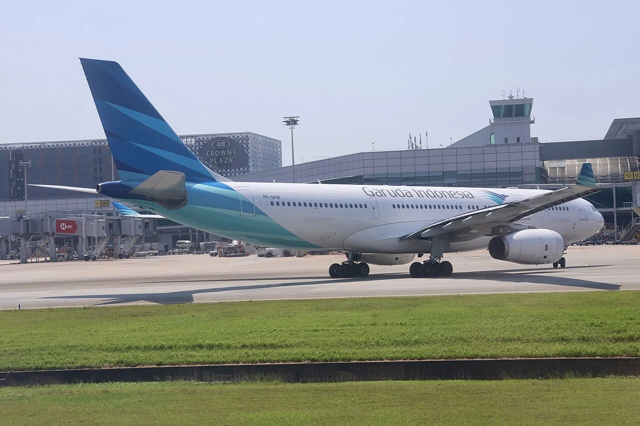 A white passenger jet with a blue-and-green tail stands beside an airport terminal.