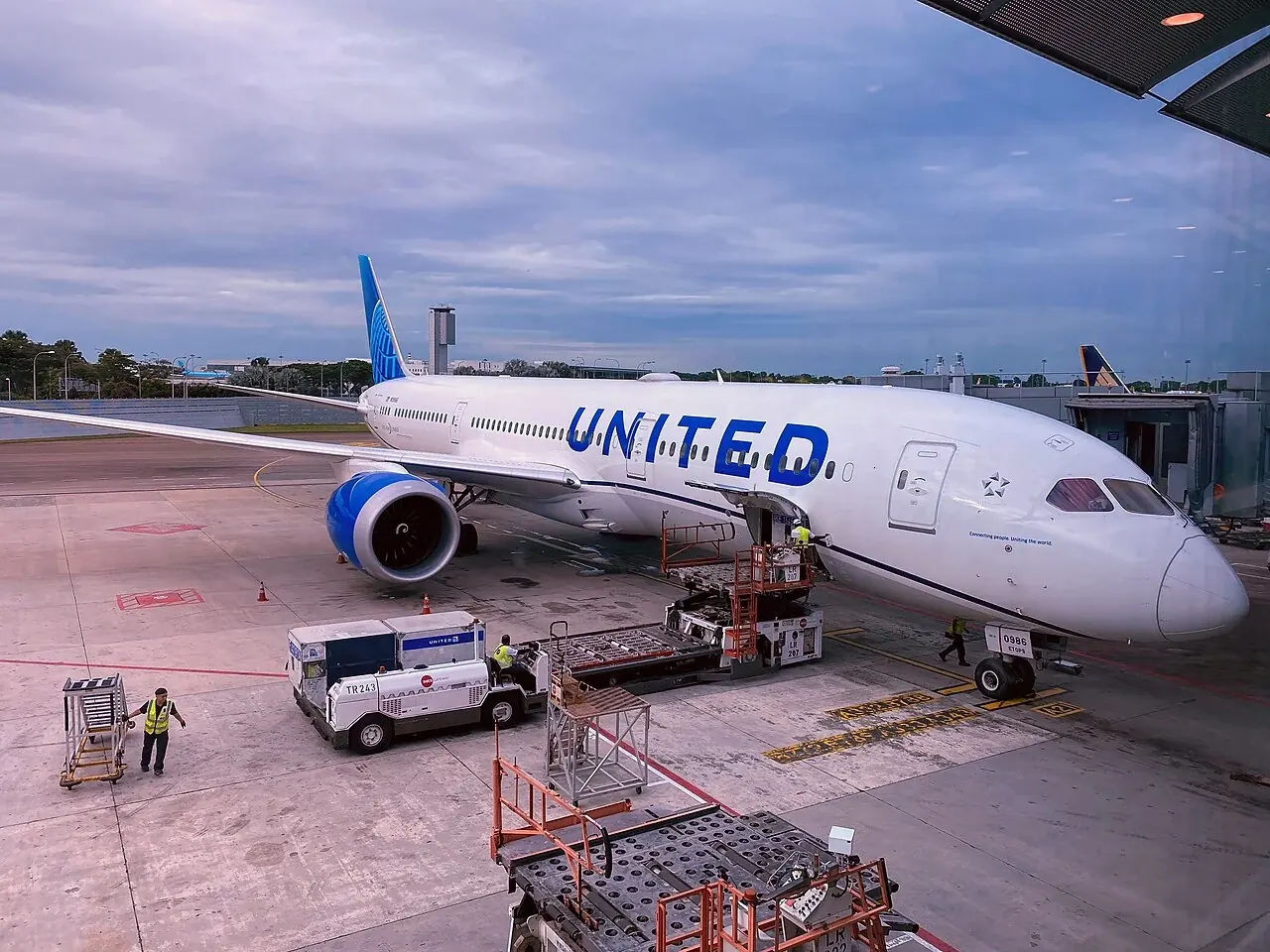 A white passenger jet with a blue tail has steps and equipment beside its nose.