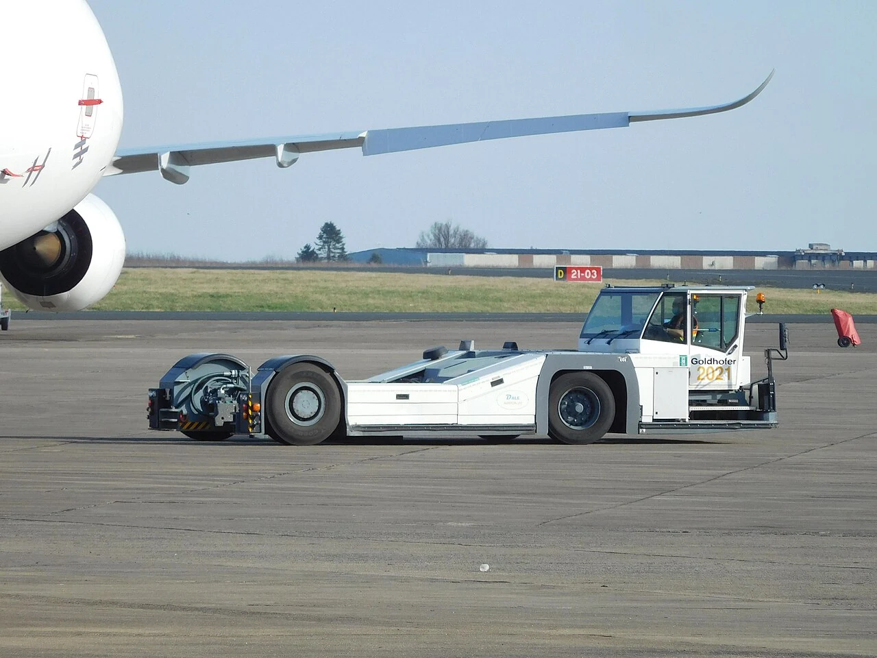 A long low aircraft tractor has large black tyres and a small cab at one end.