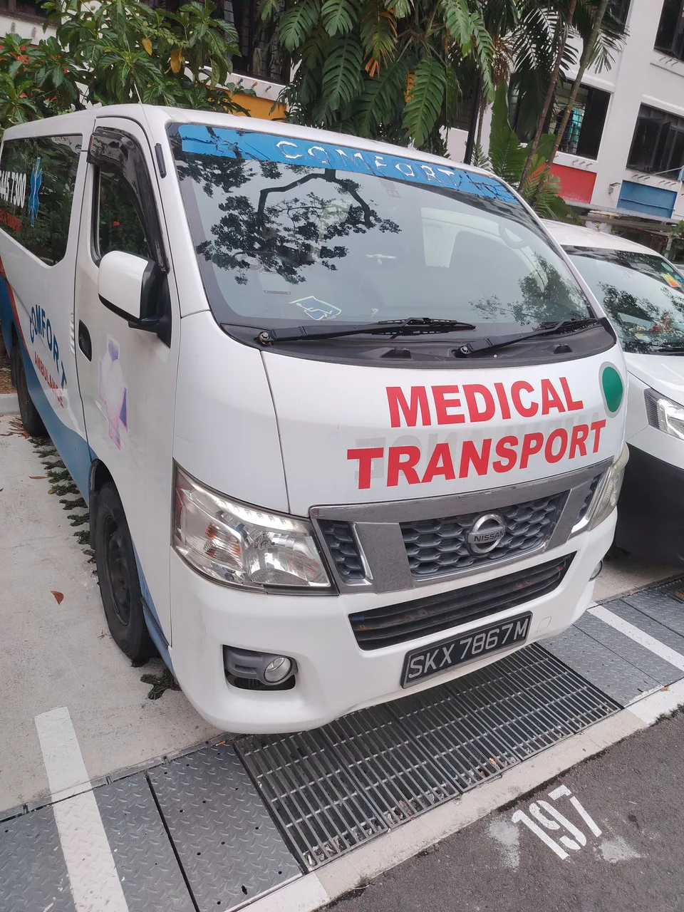 Ambulance — a white Comfort Ambulance van with MEDICAL TRANSPORT in red on the bonnet, parked in a car park, Photographed in Singapore
