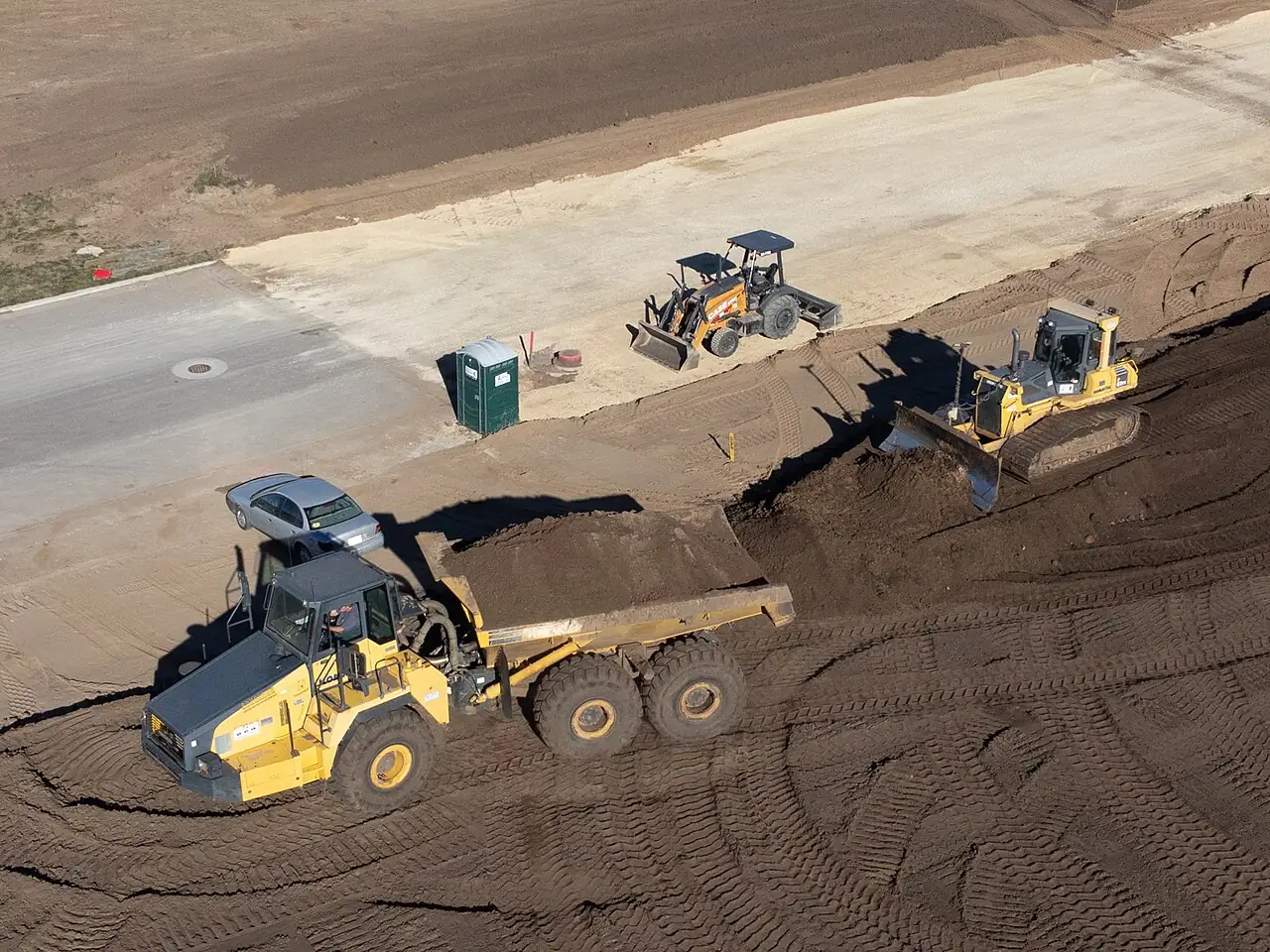 An articulated dump truck carries soil across a large building site.