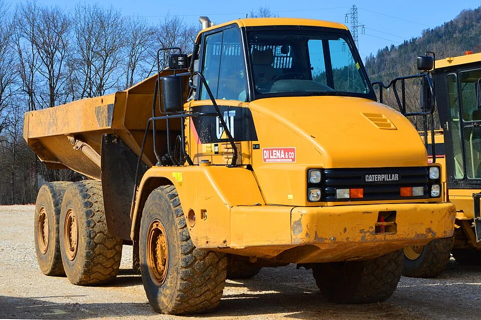 A yellow dump truck has a high cab, six large tyres and a deep rear box.