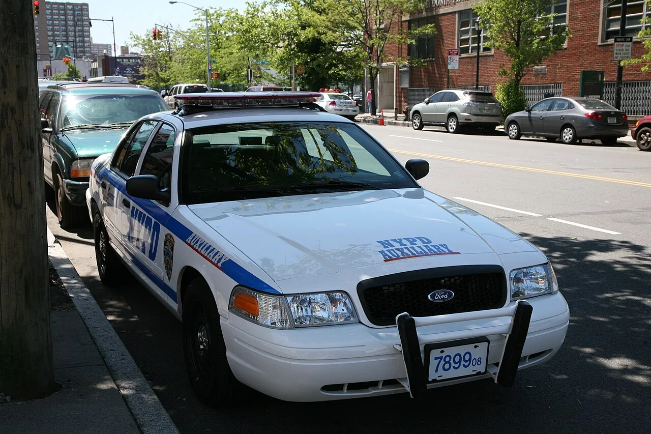 A white and blue NYPD Auxiliary car is parked beside a kerb.