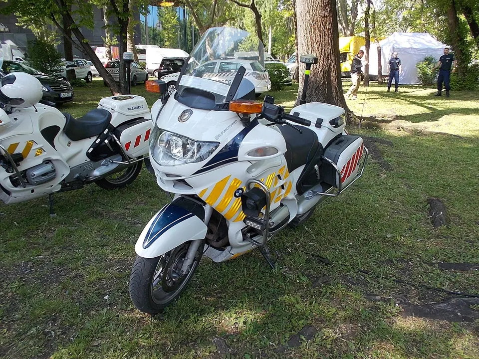 A white auxiliary police motorcycle with a tall windscreen stands on grass.
