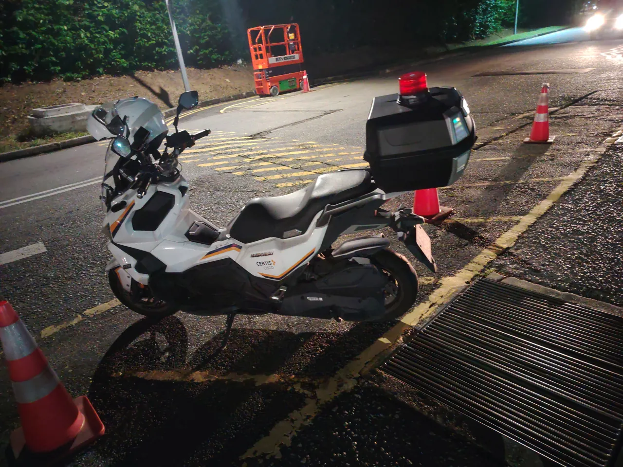 A white auxiliary police motorcycle is parked at night.